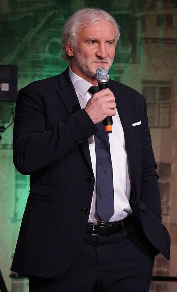 Bild på en gråhårig man med kostym som talar i mikrofon.